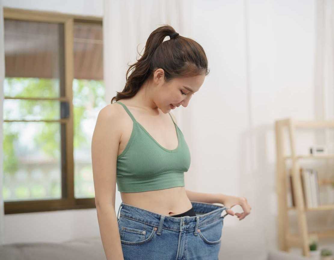A Person holding the waistband of oversized jeans, showing the weight loss achieved through consistent HIIT workouts.