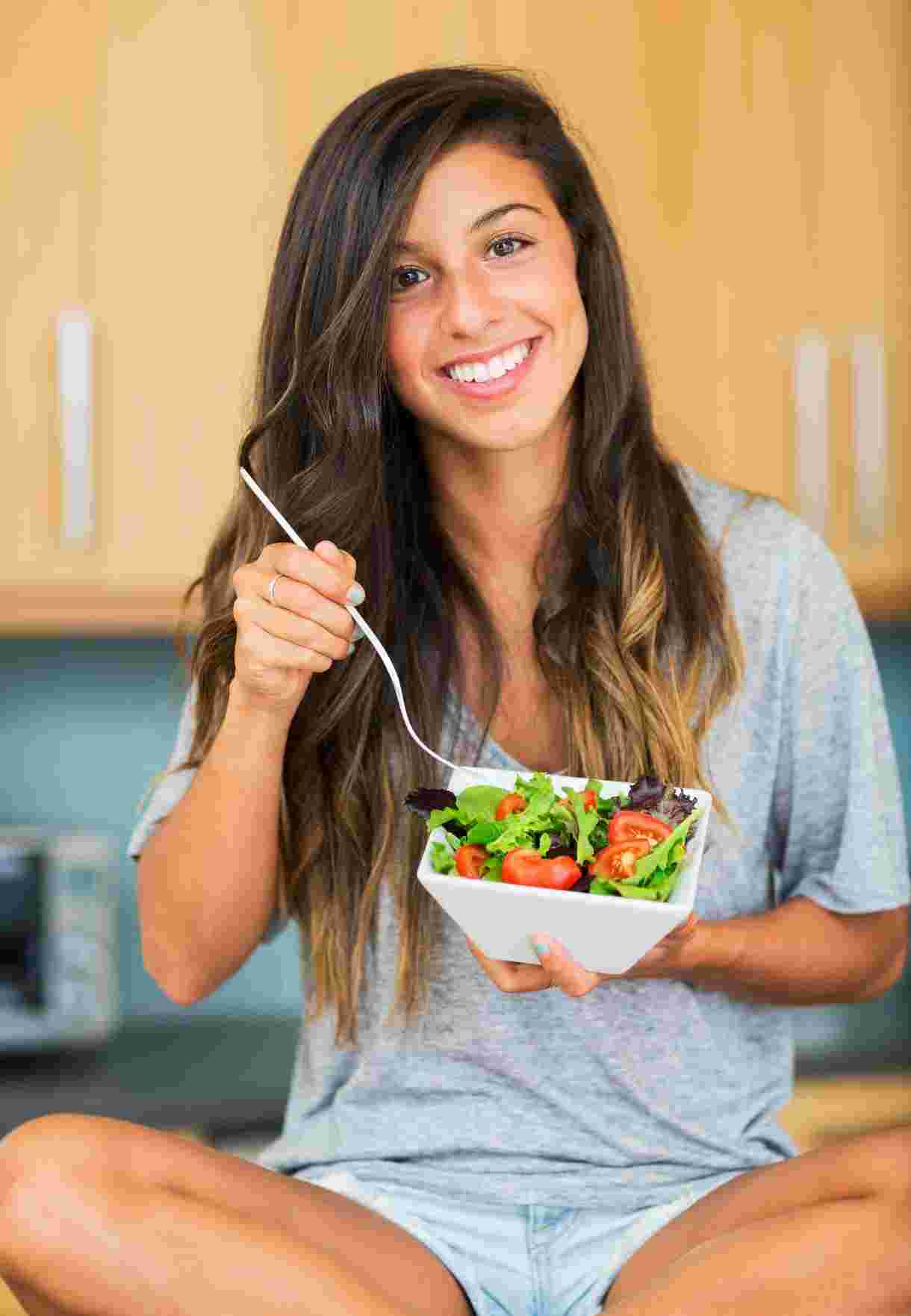 Person holding a bowl of salad with cherry tomatoes and leafy greens.
