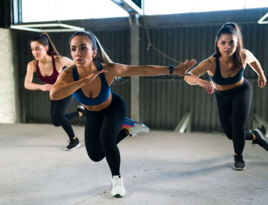 Athletes executing a powerful ice skater move in a stylish gym with large windows, showcasing dedication to high-intensity training.